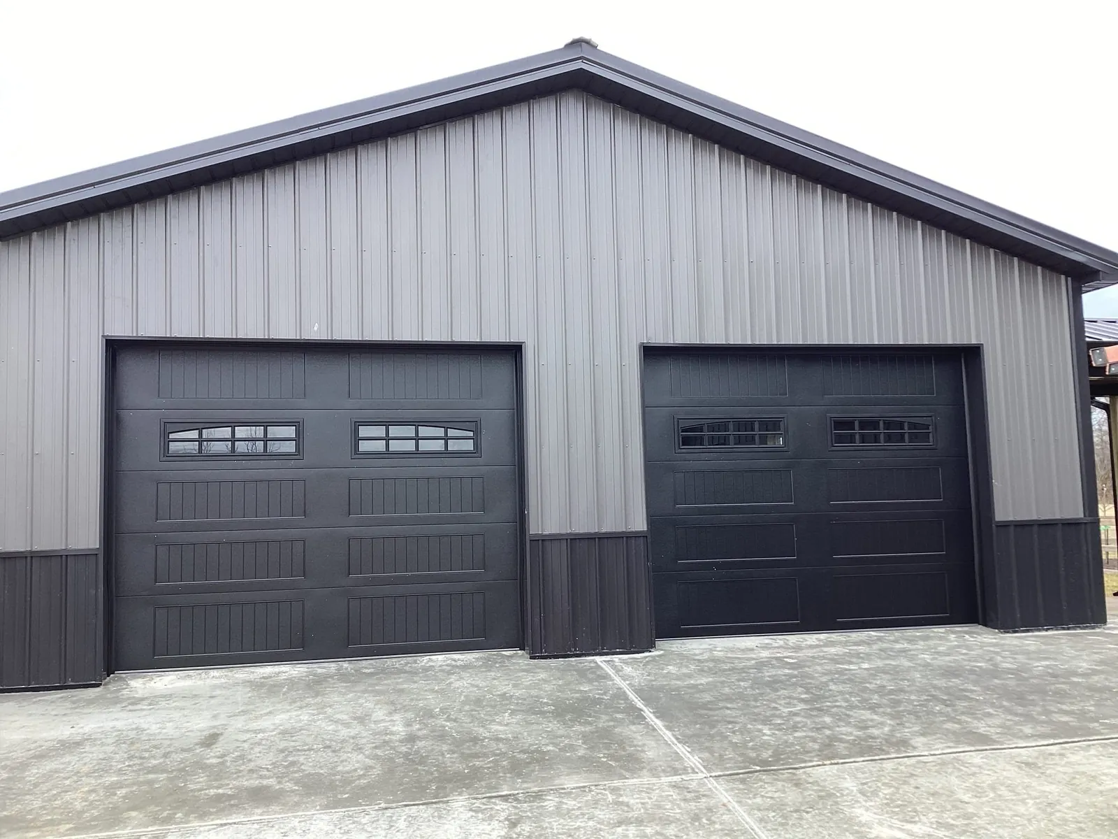 Two dark garage doors with small top windows on a gray detached garage